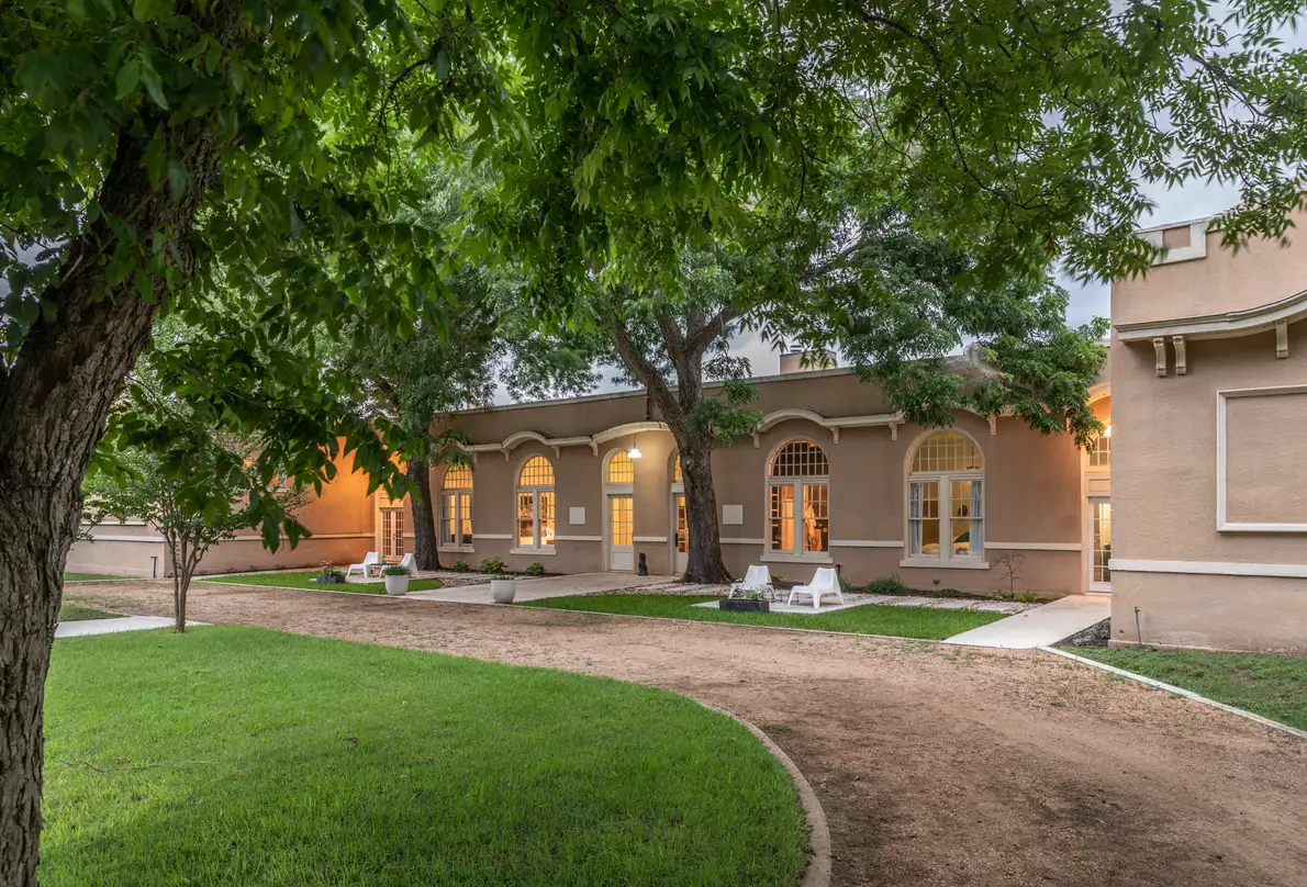 The schoolhouse at dusk, arched windows glowing warm above a lawn and gravel path