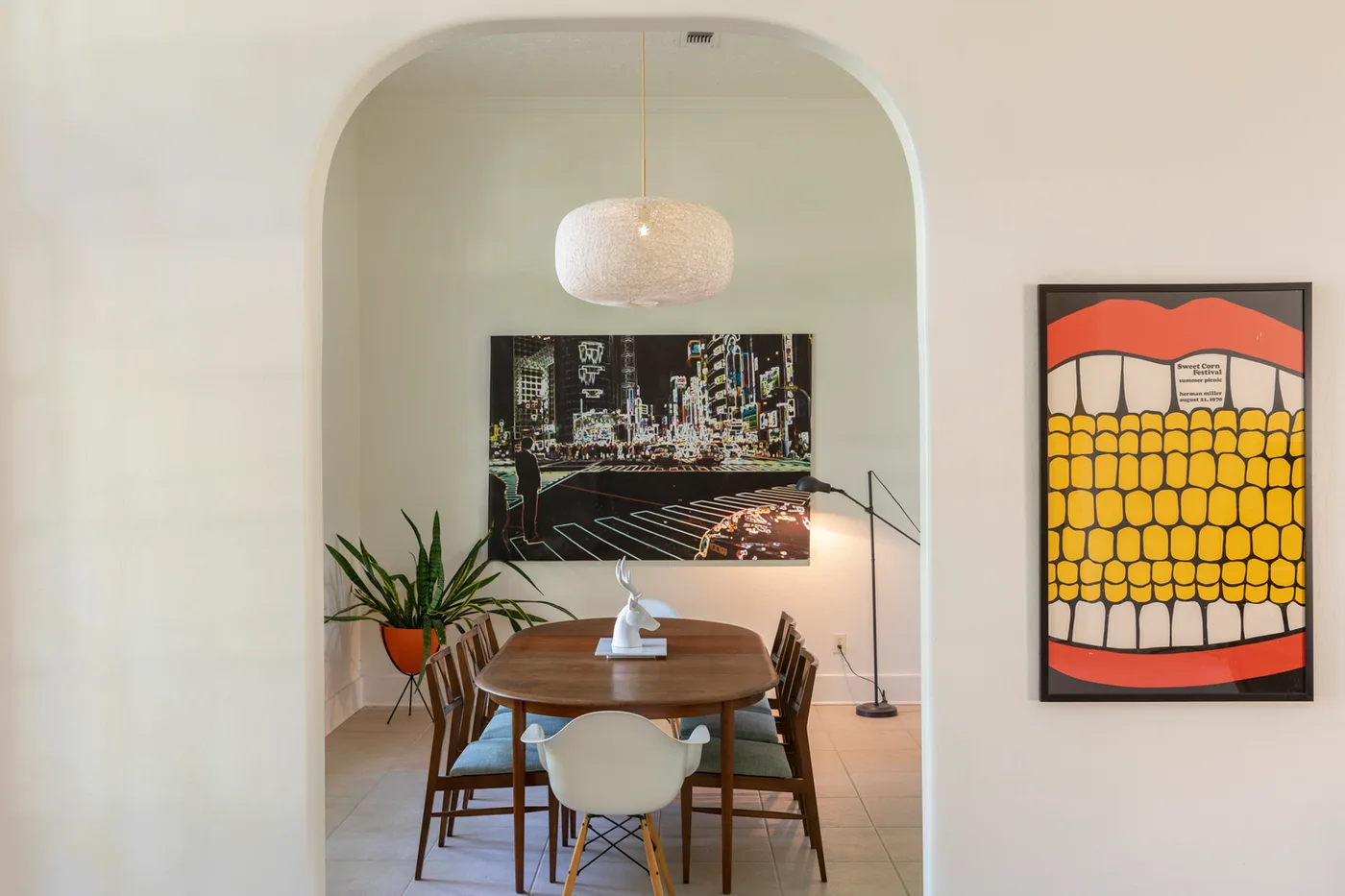 Mid-century dining table framed by a plaster archway, woven pendant light and bold pop-art prints