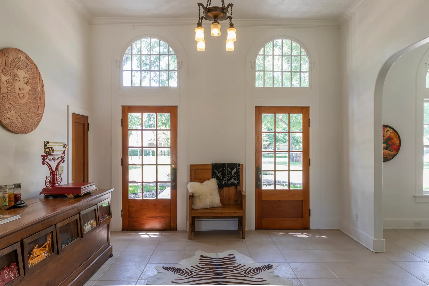 Entry hall with arched transoms above wooden doors, antique glass-front counter and zebra-hide rug