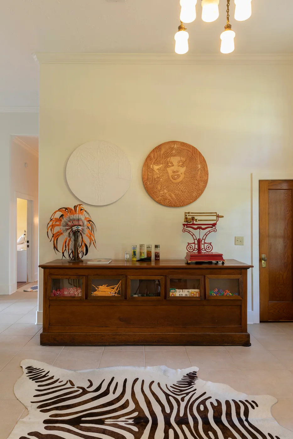 Antique glass-front display counter topped with a feathered headdress and red vintage scale, round wall art