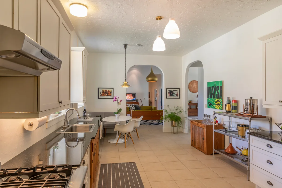 Galley kitchen with glass pendants opening through arches to a dining nook and living room