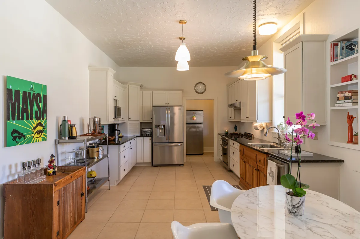 Long schoolhouse kitchen with cream cabinets, stainless appliances and a marble table with potted orchid