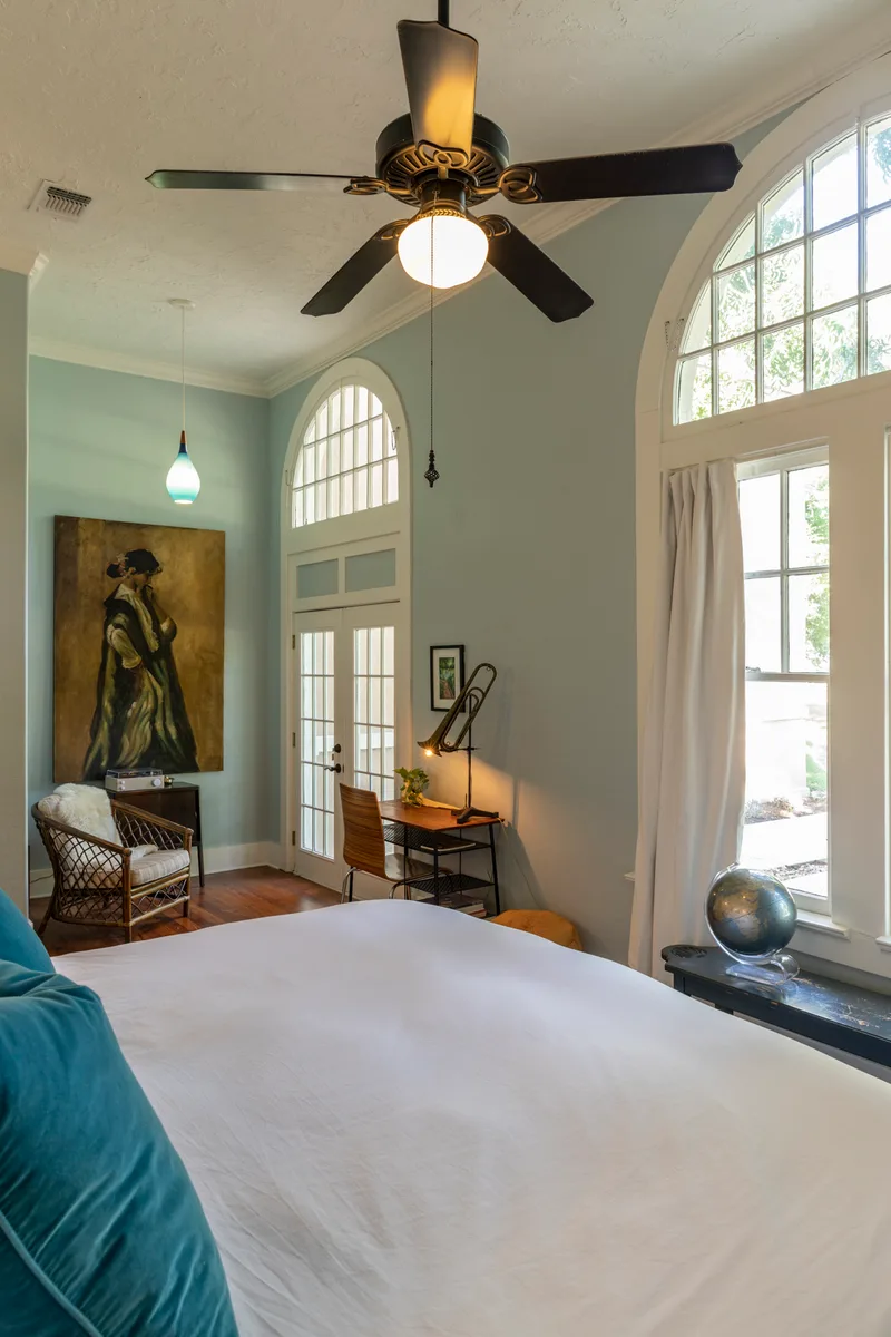 Guest bedroom with sage walls, arched windows, teal velvet pillows and a small writing desk