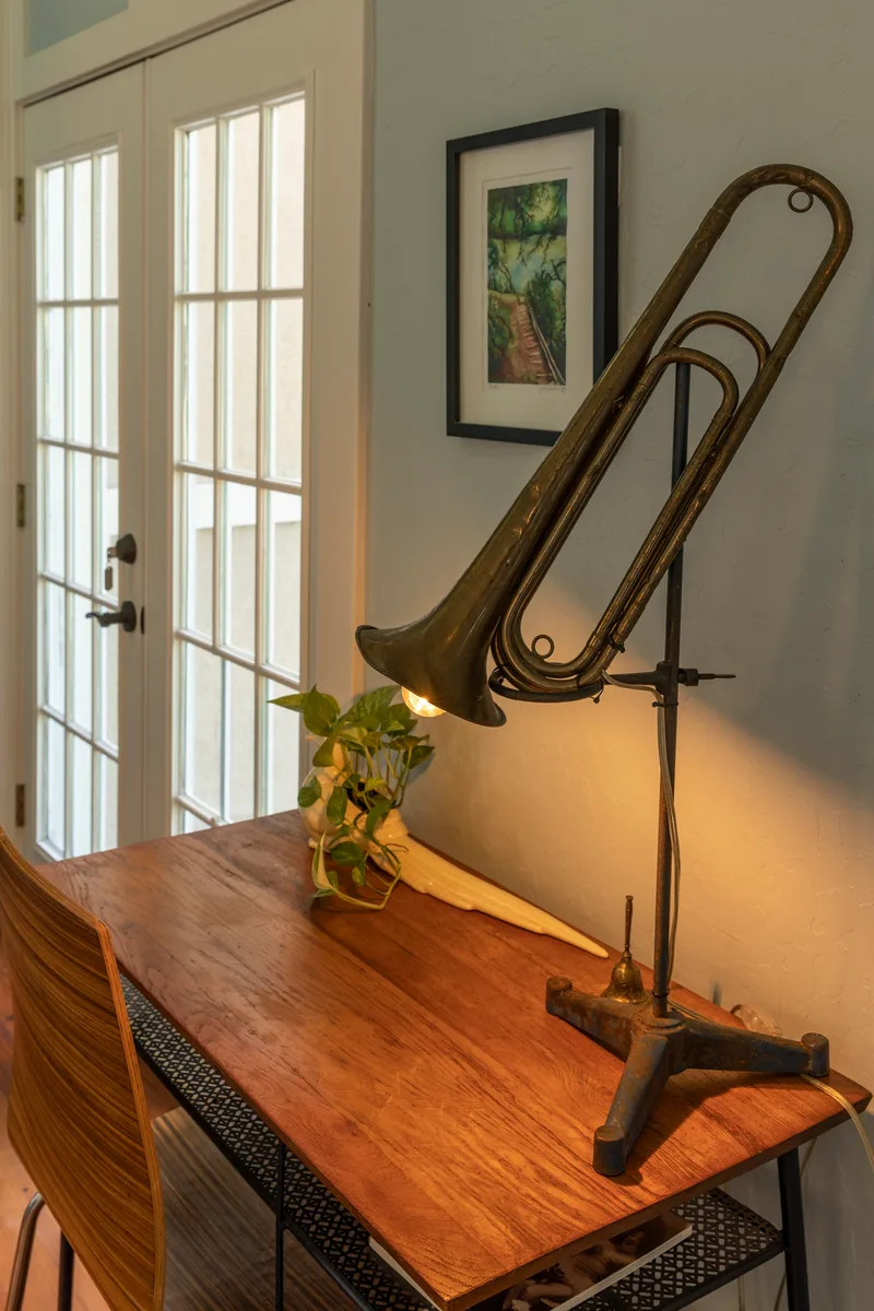 Brass horn repurposed as a lit lamp on a wooden writing desk beside French doors
