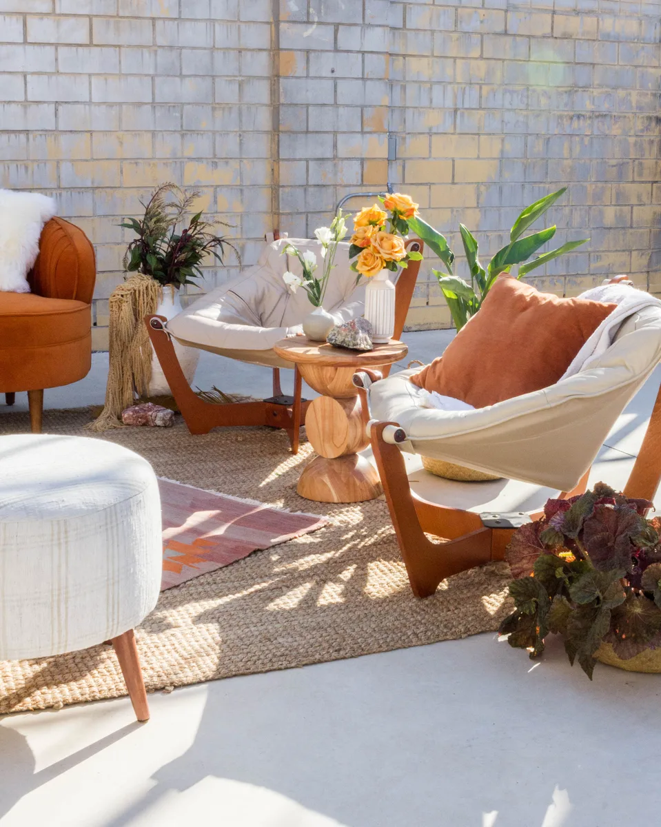 Sunlit lounge corner with canvas sling chairs, a wooden pedestal table and orange roses