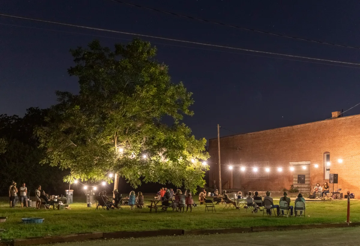 Martindale River Cafe at night: string-lit lawn, folding chairs, musicians playing beside brick wall