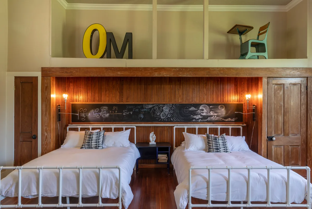 Twin iron beds against beadboard panelling below a long chalkboard lettered School's Out For Summer