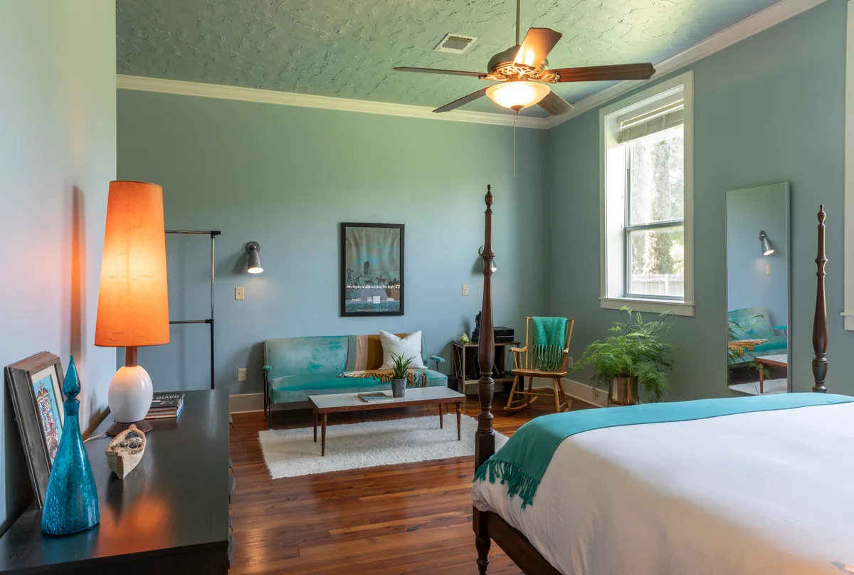 Ellison Suite with four-poster bed, teal throw, sitting area and tall orange lamp