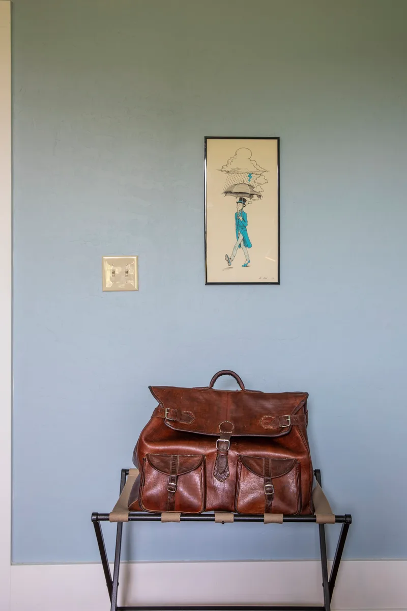Vintage brown leather duffel bag on a folding luggage rack below a framed umbrella print