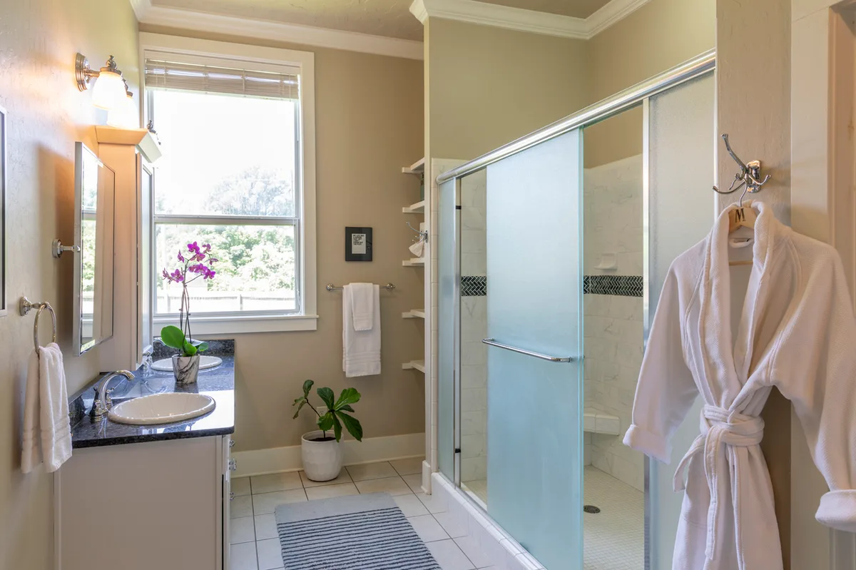 Guest bathroom with granite vanity, glass shower, white robe on a hook and an orchid