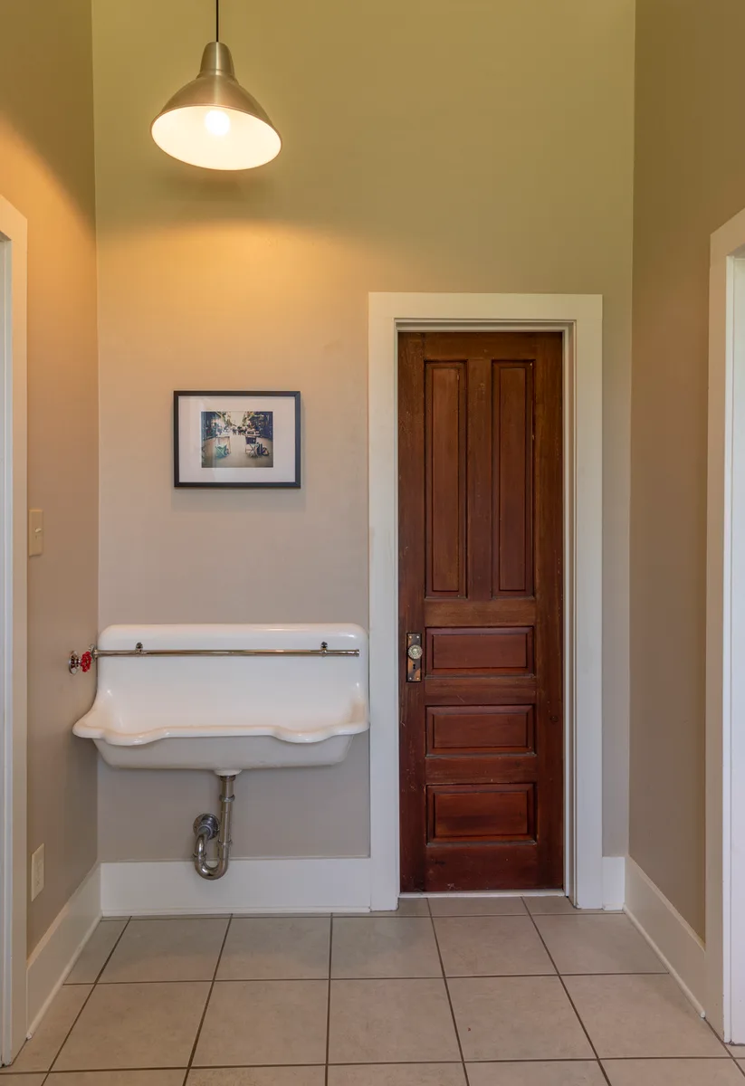 Original gymnasium urinal, a long white porcelain trough with exposed plumbing beside a tall wood door