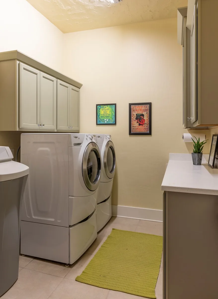 Laundry room with side-by-side washer and dryer, lime green rug and framed prints