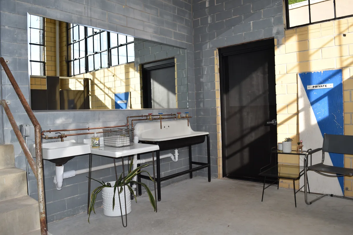Vintage white sinks with exposed copper plumbing and a long mirror in a grey block washroom