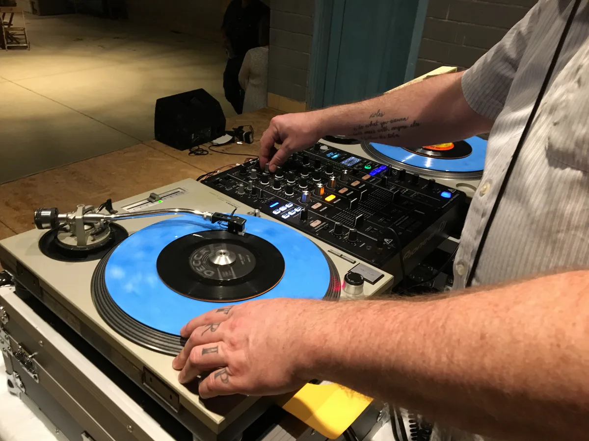 DJ's hands on twin turntables and a mixer, a blue vinyl record on the platter