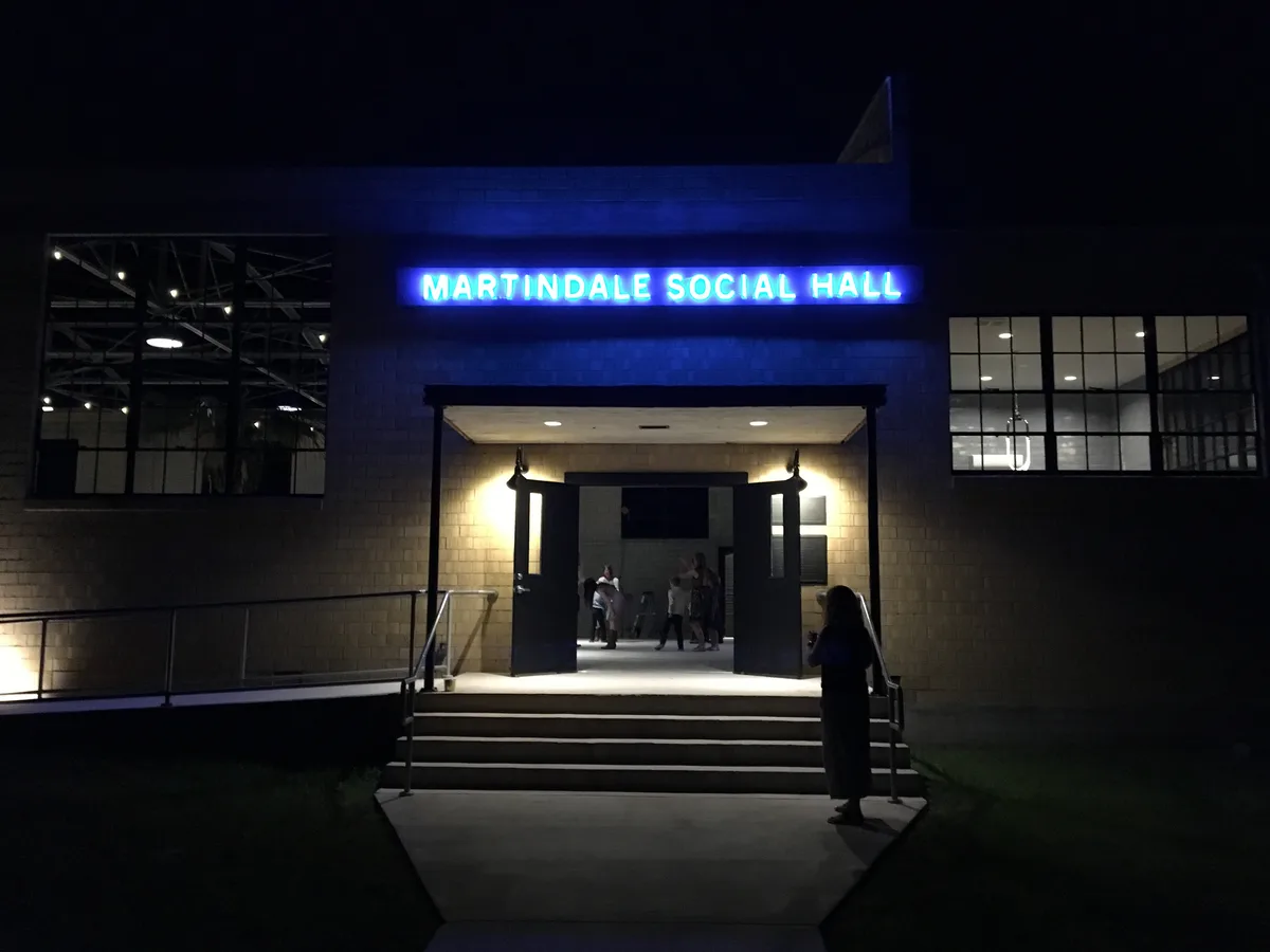 Blue neon Martindale Social Hall sign glowing above lit entrance doors at night