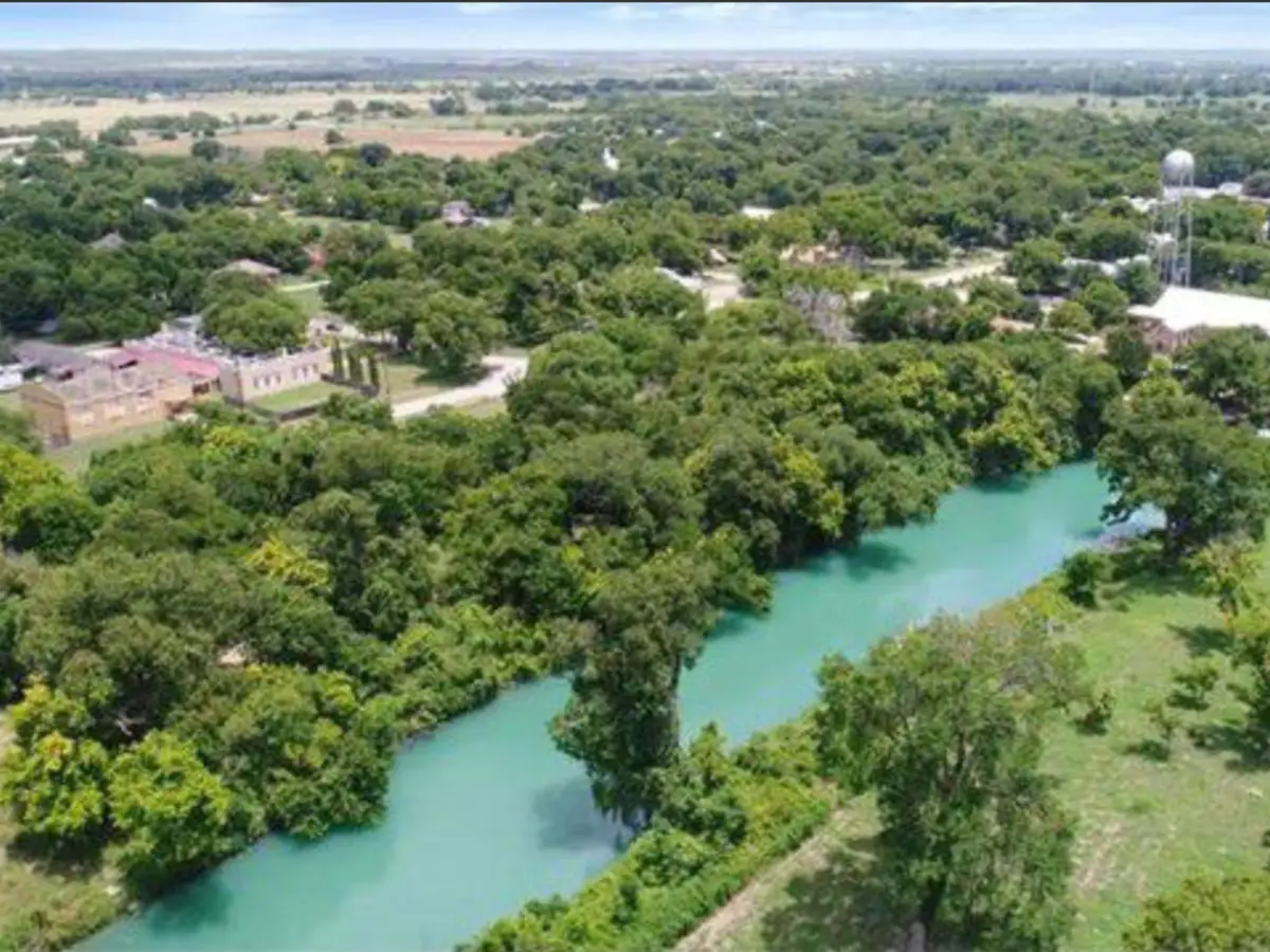 Aerial view of the turquoise San Marcos River winding through trees beside small-town Martindale