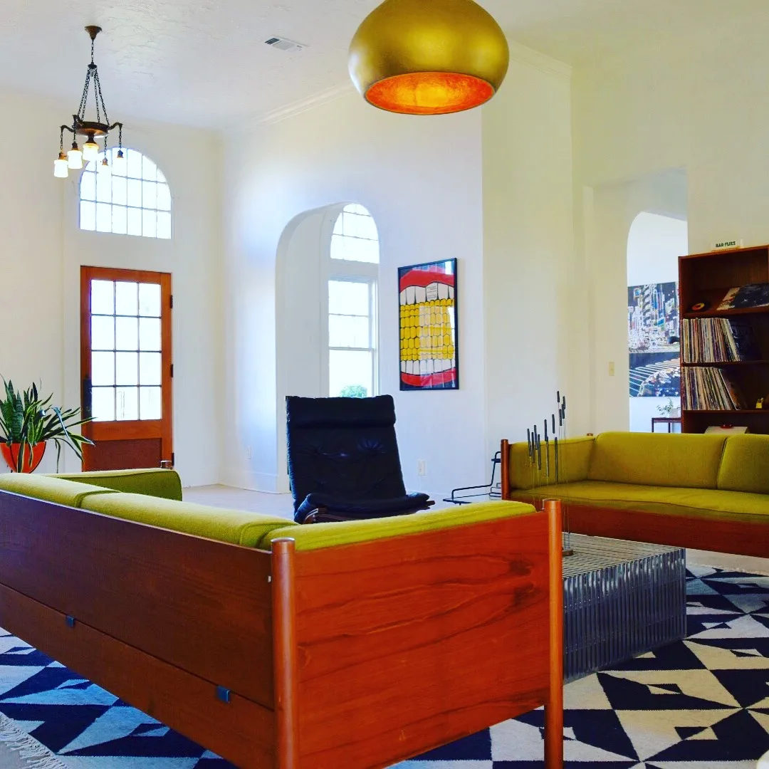 Living area with chartreuse teak sofas, a brass dome pendant and tall arched windows