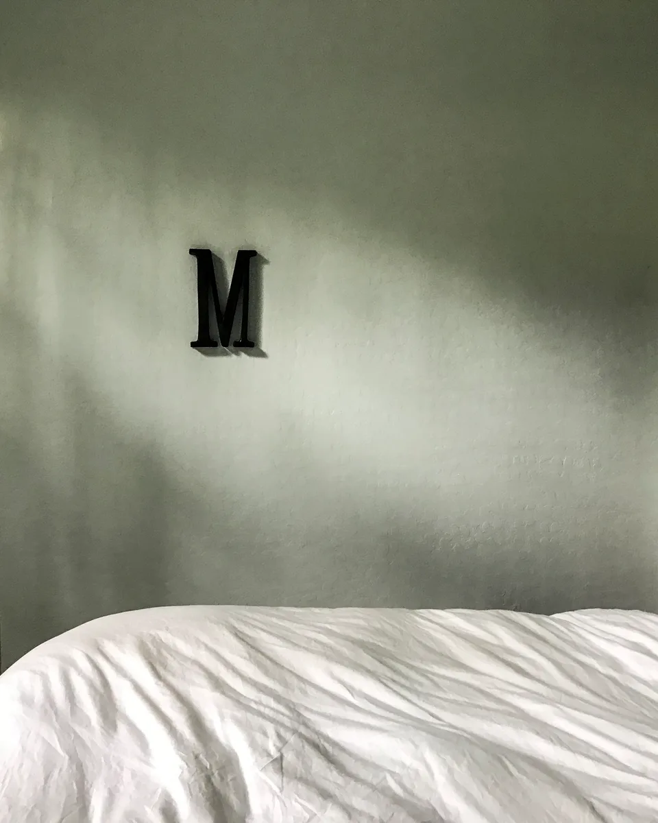 Lady Martindale room, a black letter M on a sage wall above rumpled white bedding
