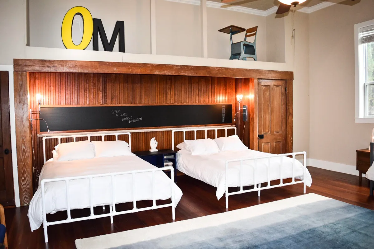 Harper Hall's two white iron beds against dark beadboard with a chalkboard rail above
