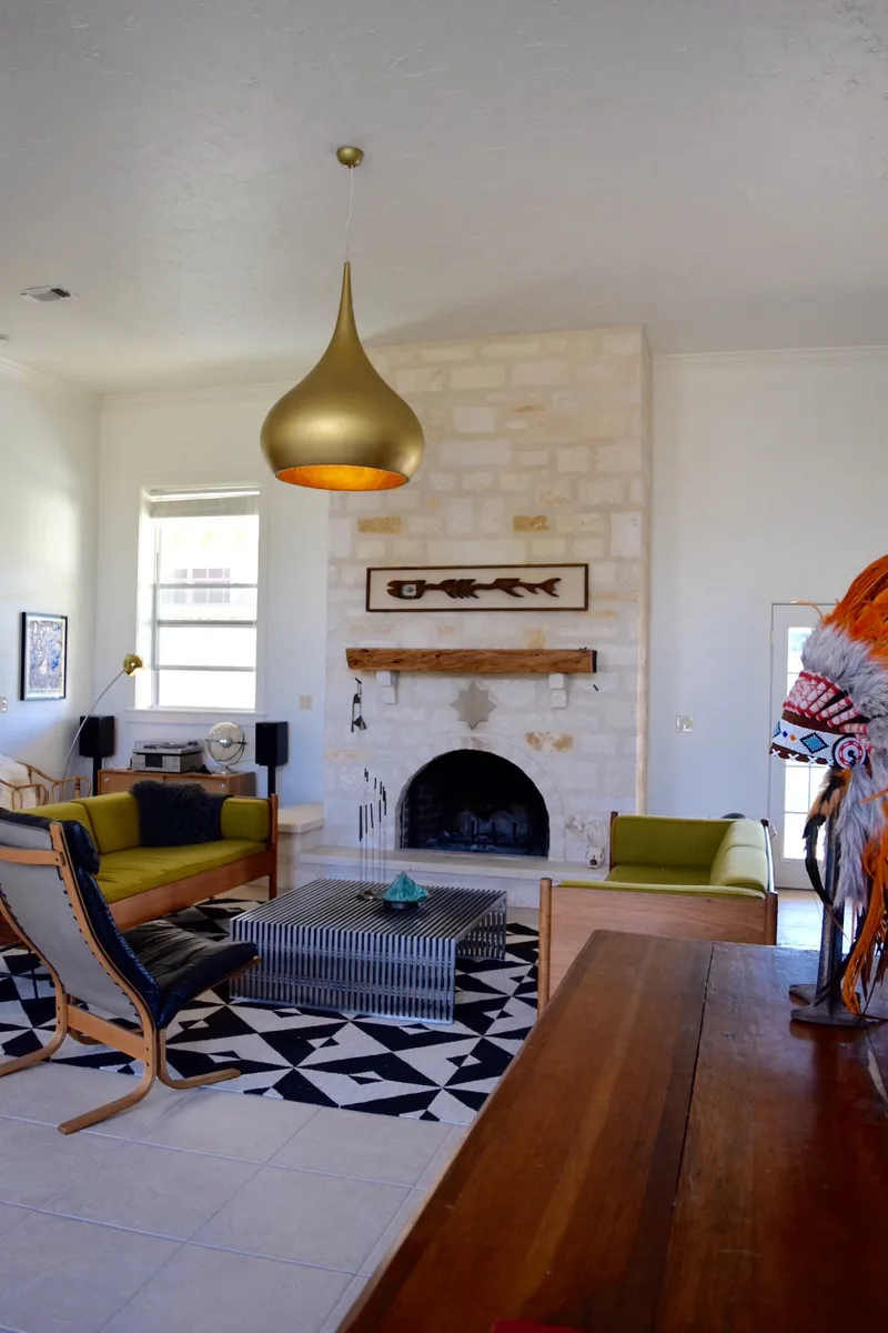 White limestone fireplace with a timber mantel, olive sofas and a bold geometric rug