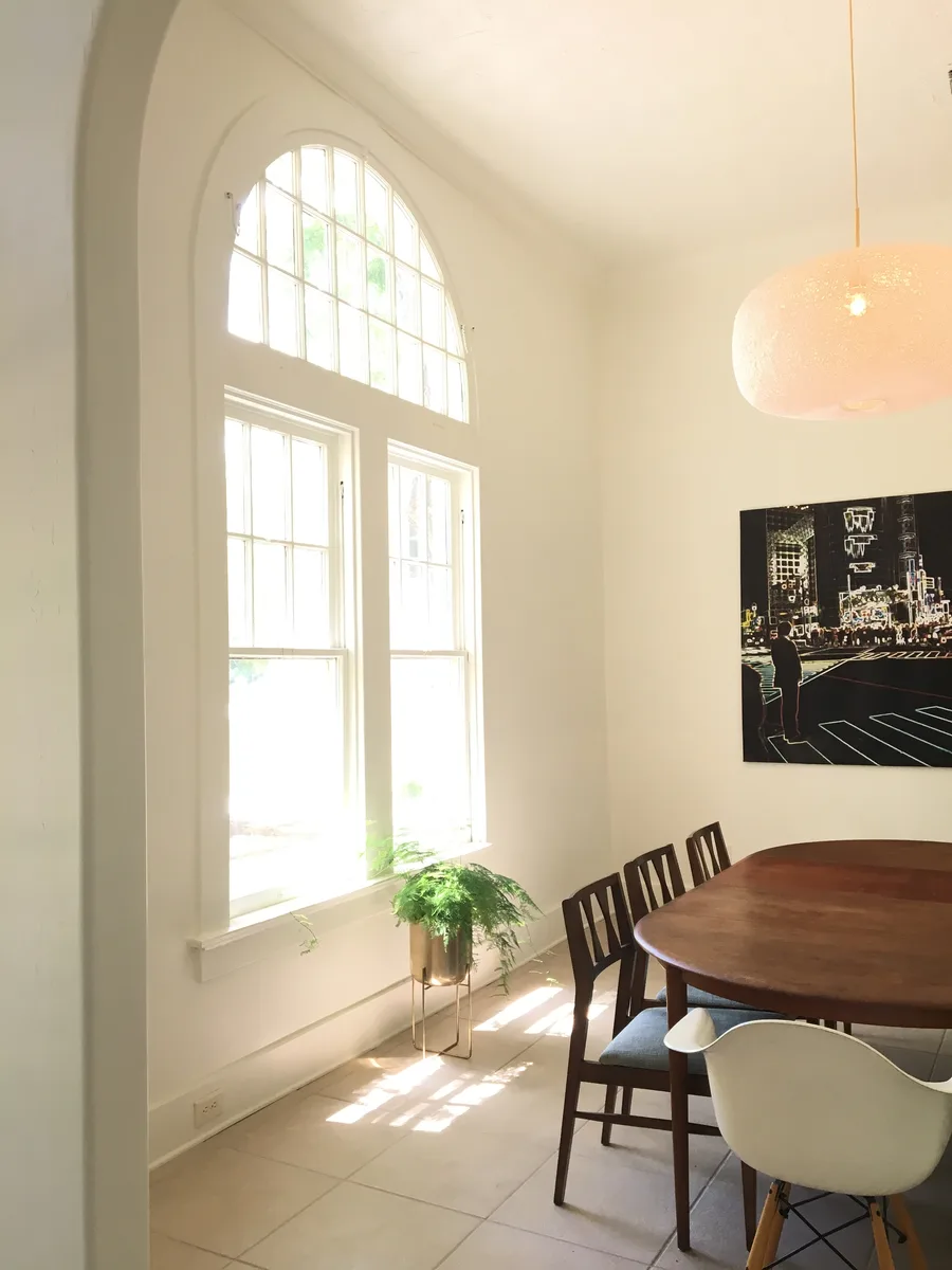 Dining area with oval walnut table, arched multi-pane window, pendant lamp and potted fern
