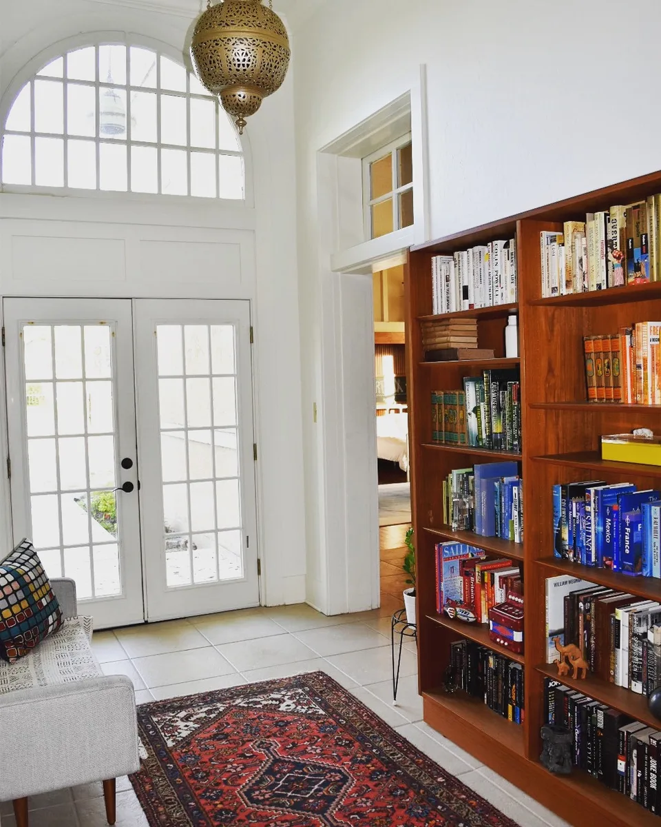 Library corner with tall teak bookshelves, French doors, arched fanlight and a red Persian rug