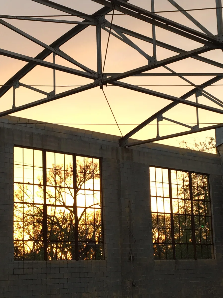 Steel roof trusses and tall windows in the open-air Social Hall at golden sunset