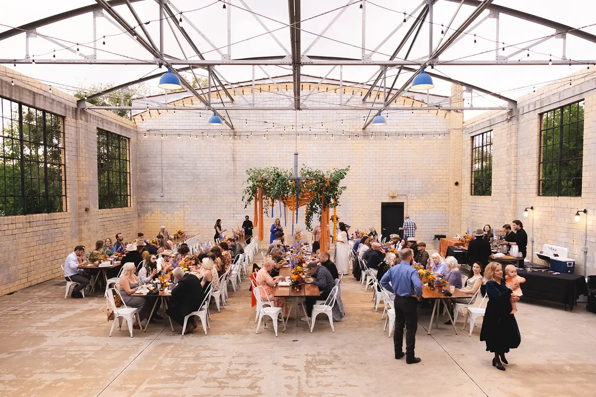 Wedding reception in the open-air Social Hall, guests at long tables beneath steel roof trusses and string lights