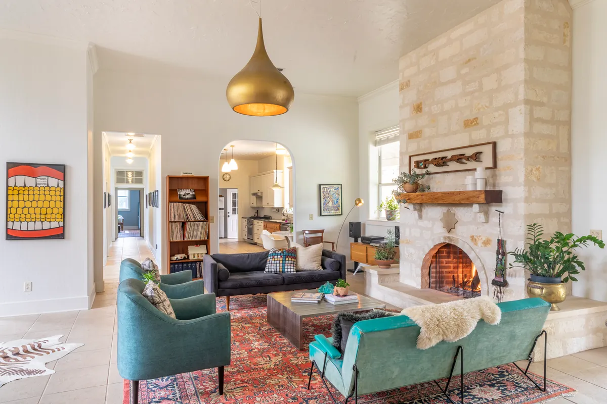 Living room looking through an arched doorway to the kitchen, a teal velvet sofa with a sheepskin throw beside the fireplace