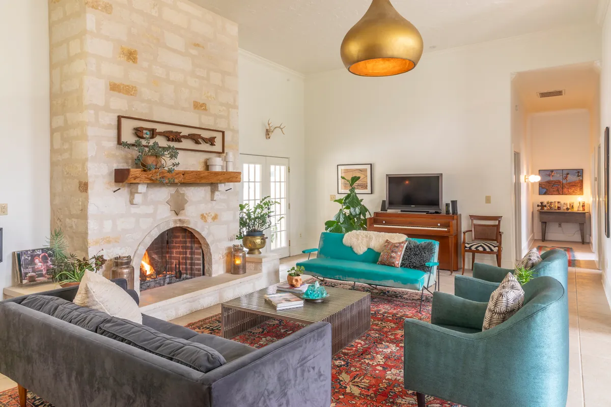 Charcoal velvet sofa and teal armchairs around a slatted metal coffee table facing the lit limestone fireplace