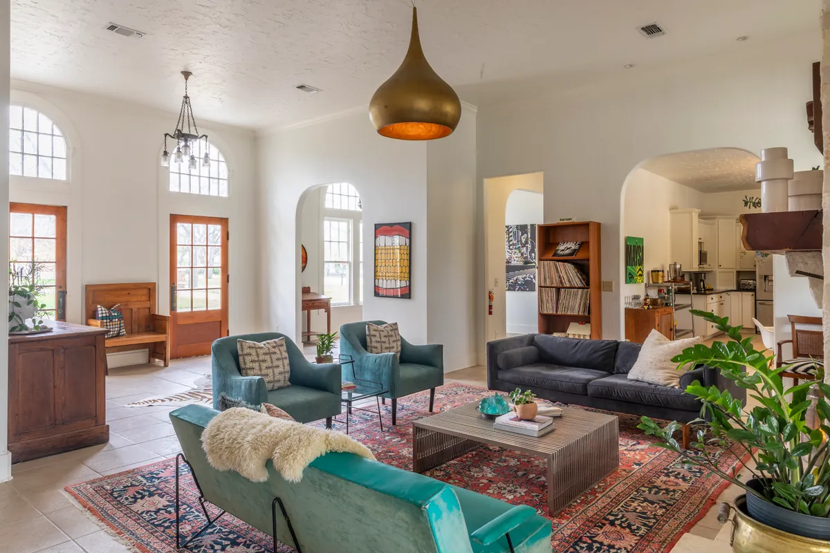 Wide view of the living room toward arched windows and wooden doors, teal chairs, charcoal sofa and a large potted plant