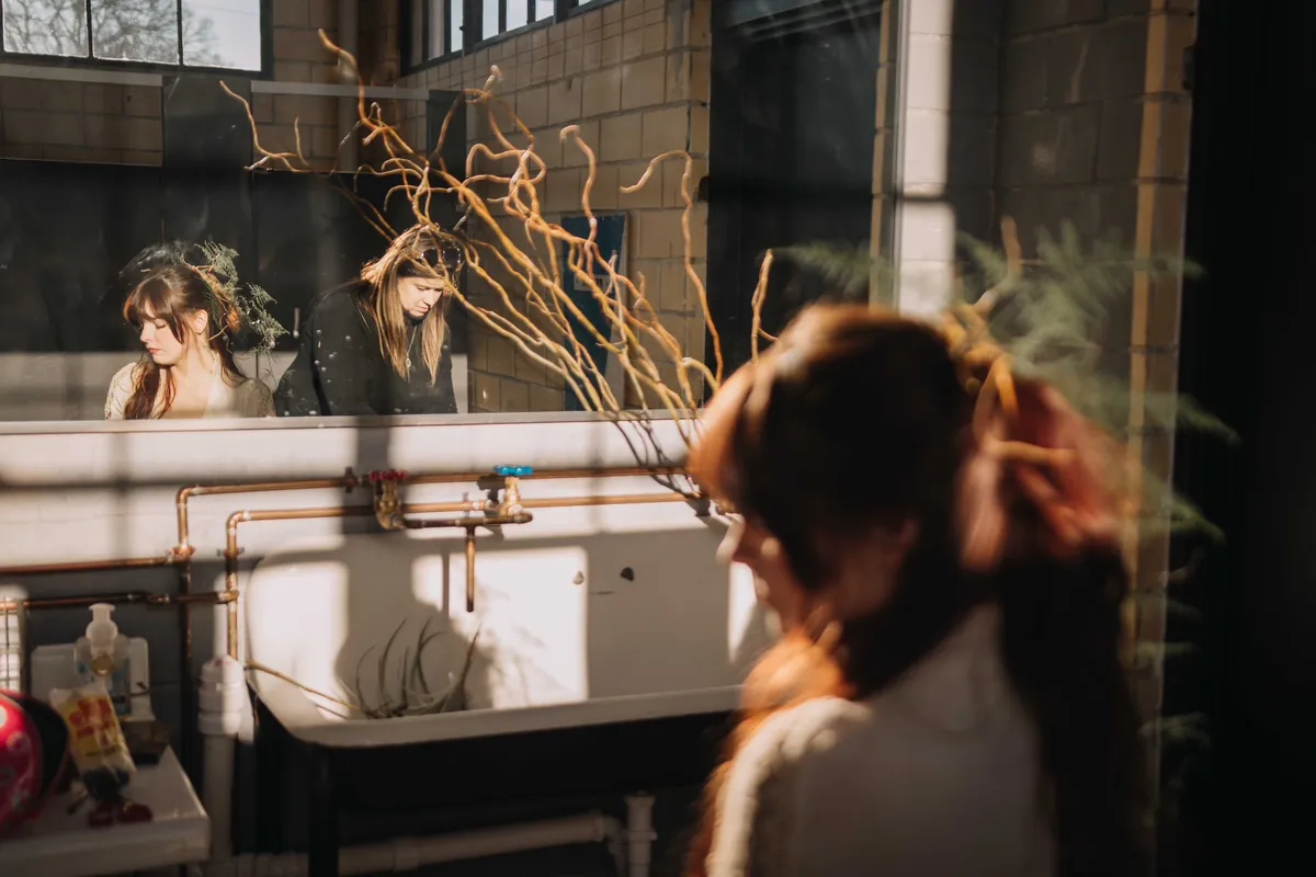 Women by the vintage sink and long mirror in the Social Hall washroom, lit by low sun through the windows
